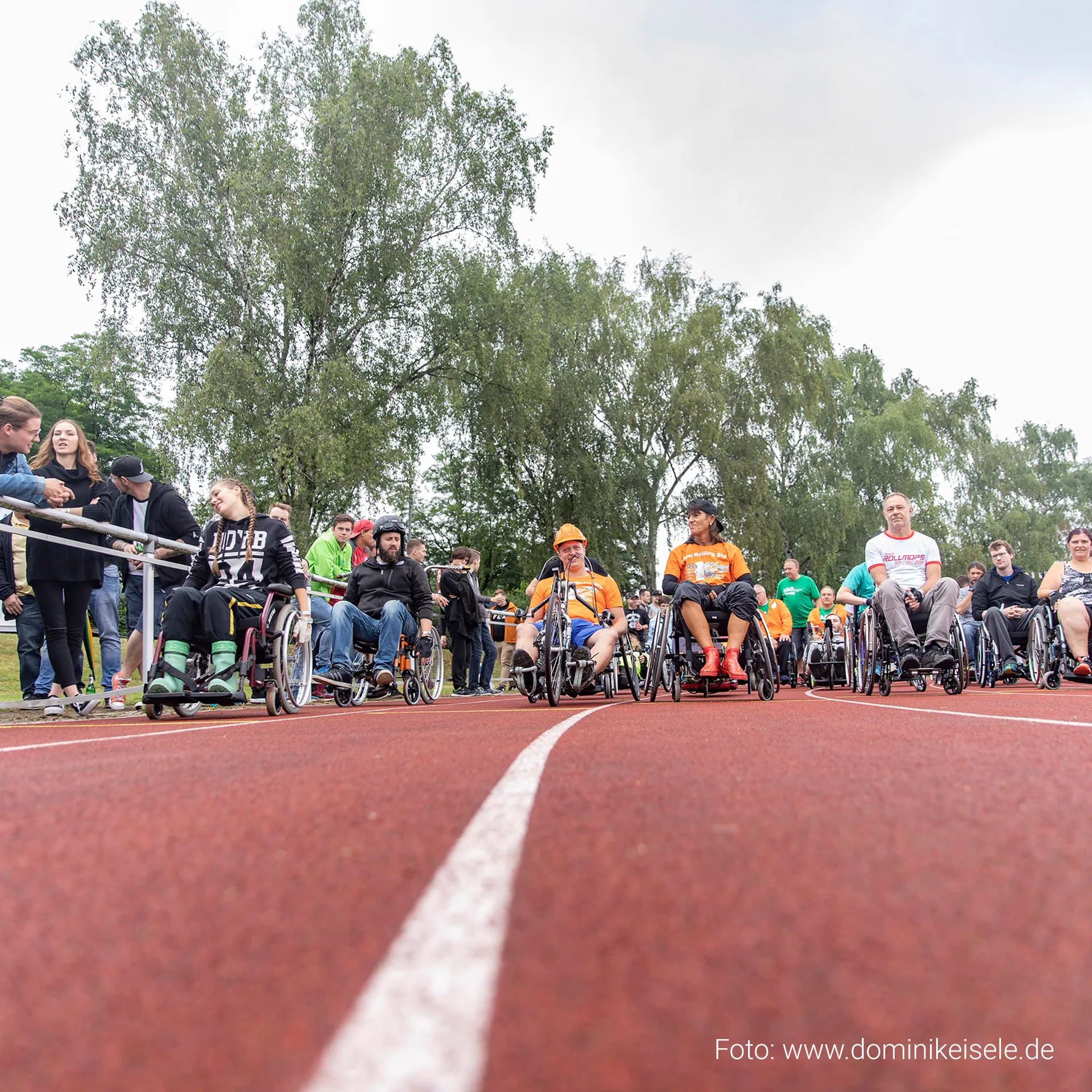 Fotografie: 24-Stunden-Rollstuhlrennen Eislingen – Inklusiver Sport für Menschen mit und ohne Behinderung Teilnehmende in Rollstühlen auf der Laufbahn eines inklusiven Sportevents im Eichenbachstadion Eislingen. Zuschauerinnen und Zuschauer verfolgen das 24-Stunden-Rollstuhlrennen, das Begegnung, Bewegung und gesellschaftliche Teilhabe fördert. Bild von Fotograf Dominik Eisele.