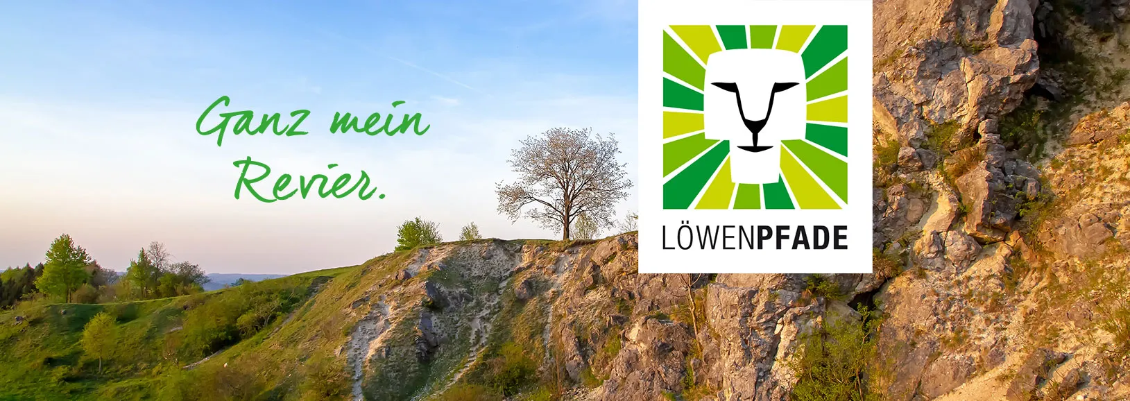 Landschaft mit grünen Hügeln, einem einsamen Baum und einem schmalen Pfad. Im Vordergrund das Logo von Löwenpfade: ein stilisierter Löwenkopf in grün-gelb-weißen Streifen mit dem Schriftzug LÖWENPFADE. Dazu der Slogan: Ganz mein Revier.